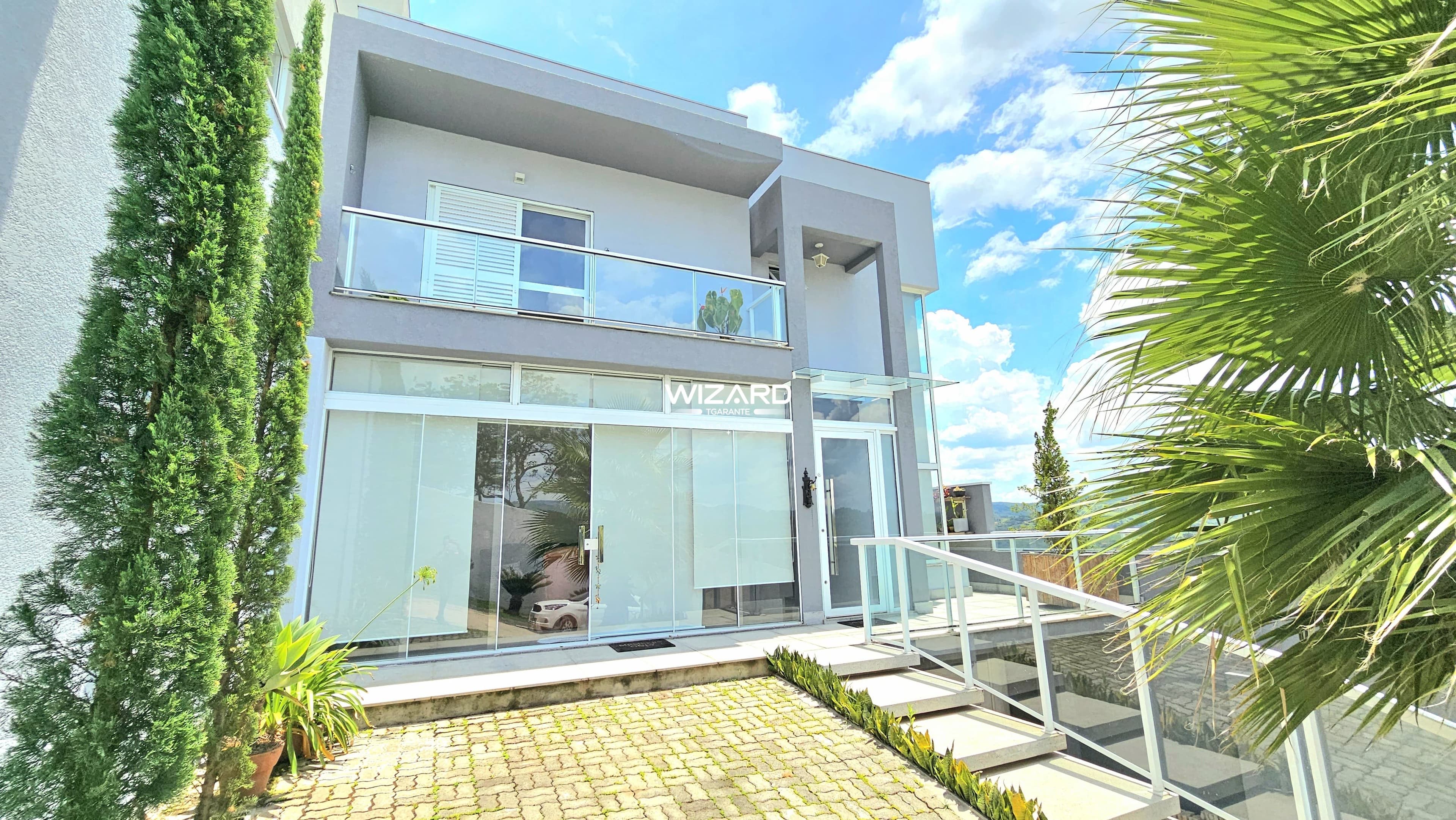 Fachada de casa moderna com varanda envidraçada, escada externa e paisagismo.