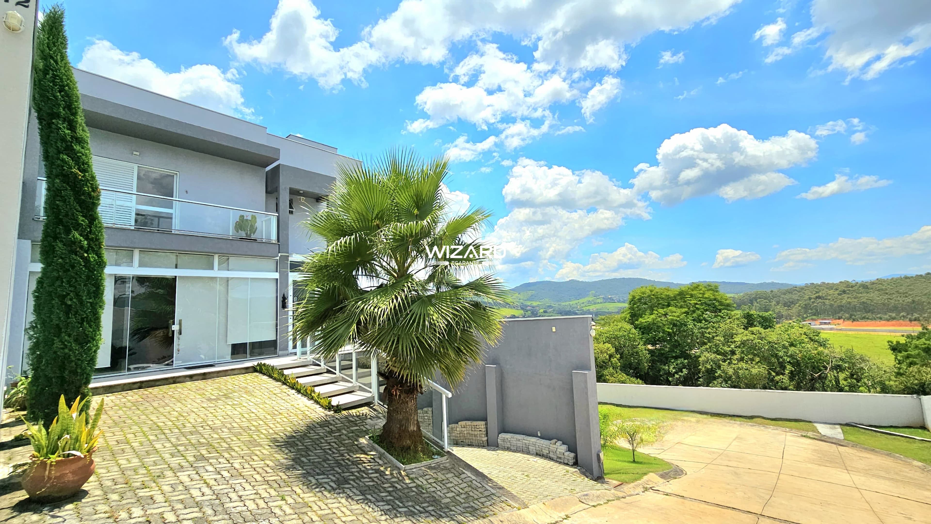 Fachada de casa moderna com palmeira, piso de bloquete e vista para área verde e montanhas.