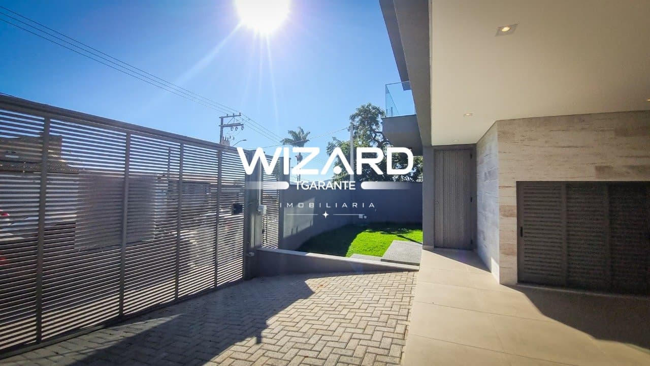 Entrada da garagem com portão de metal e acesso ao quintal gramado.